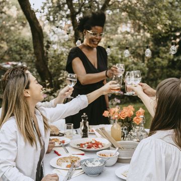smiling woman toasting drinks with friends over table during social gathering